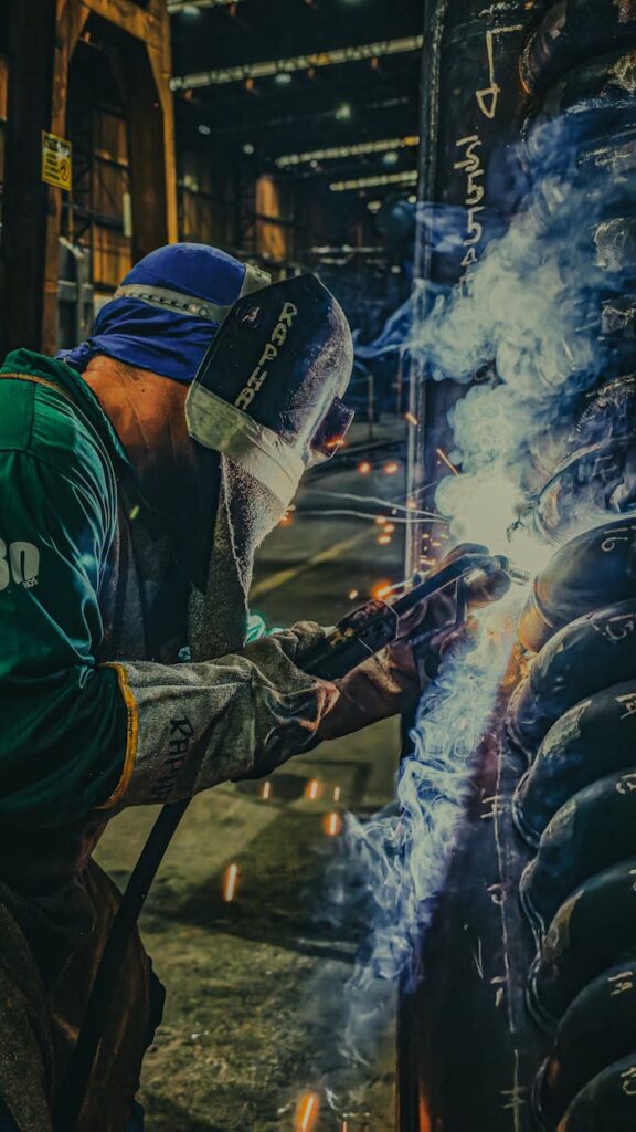 Skilled welder working in a factory, showcasing sparks and safety gear during metal fabrication.